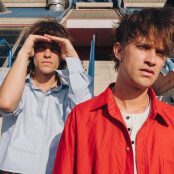 Two people one with a button down shirt pn and another with a red back standing on steps.